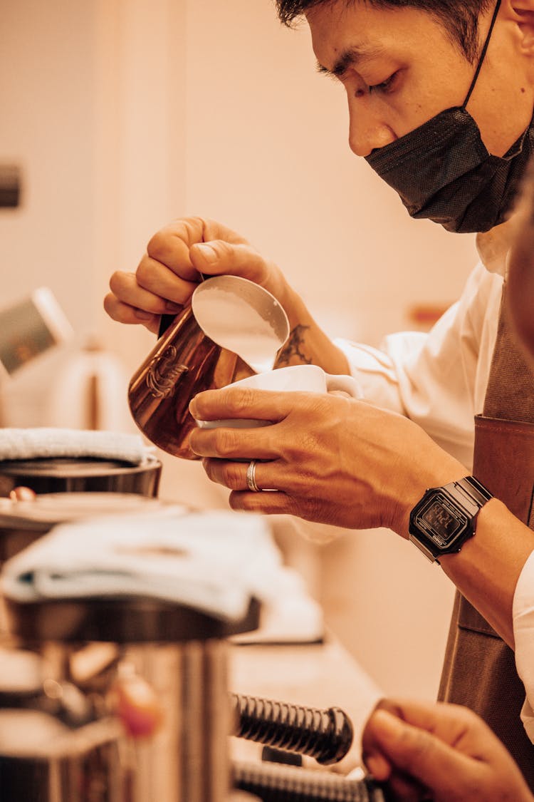 A Man Wearing Face Mask While Pouring Milk On A Cup