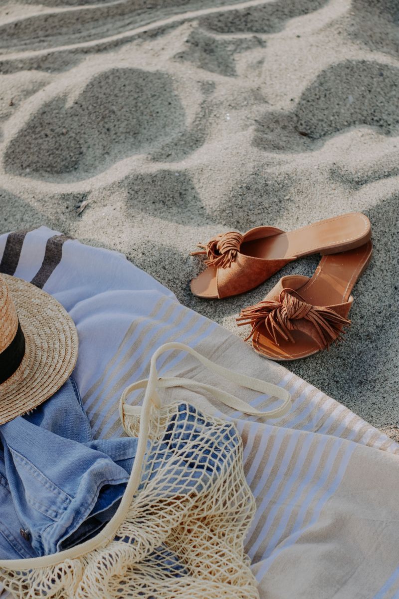 Sandals, a sun hat and a net bag laid out on warm sand
