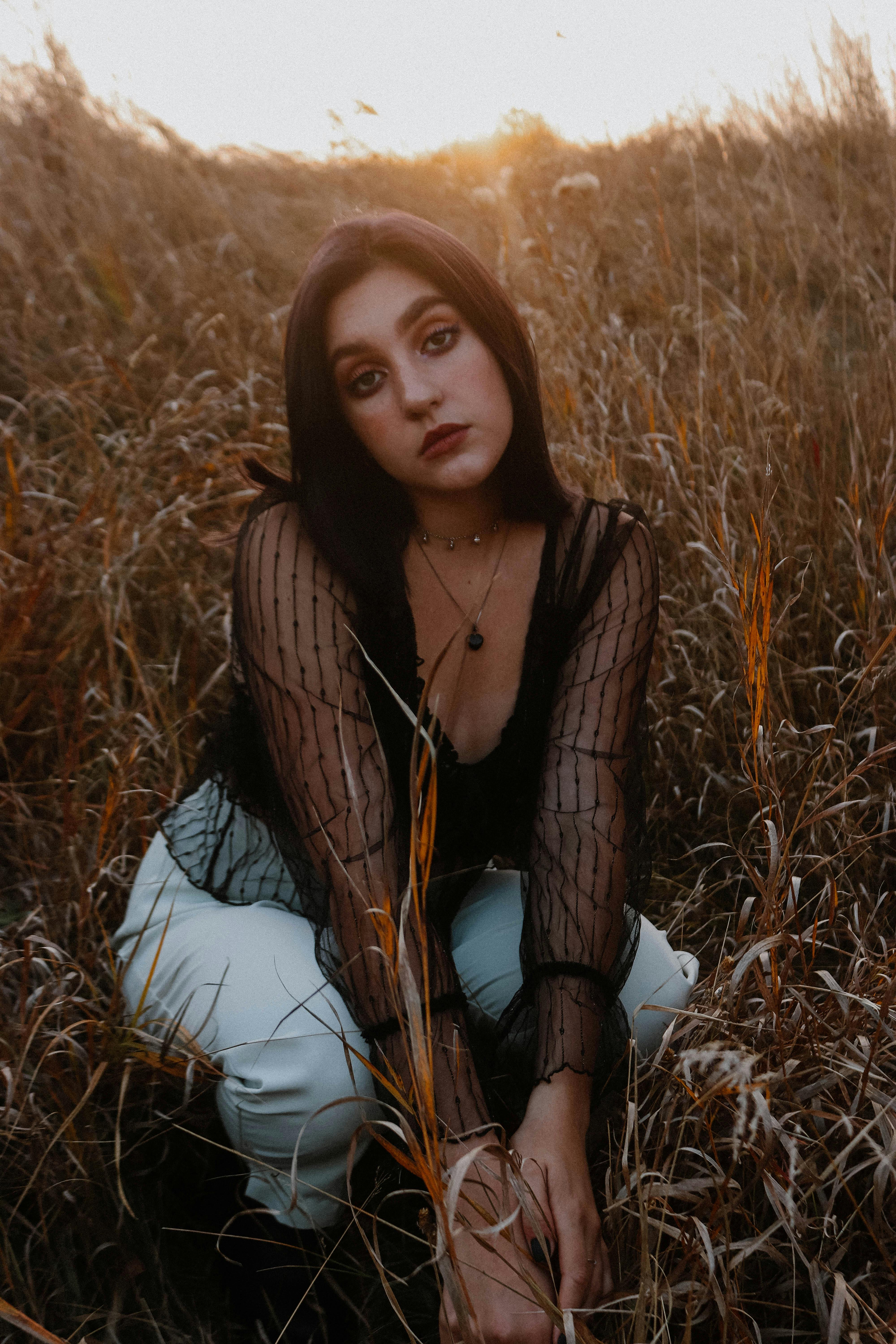 Young woman in a black blouse posing with a stylish expression in a grassy field at sunset.