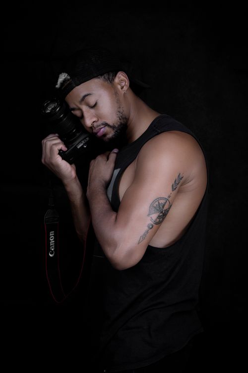 Free Dark studio portrait of a tattooed man holding a camera with eyes closed. Stock Photo