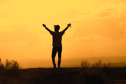 A Silhouette of a Man Standing on the Field during Sunset