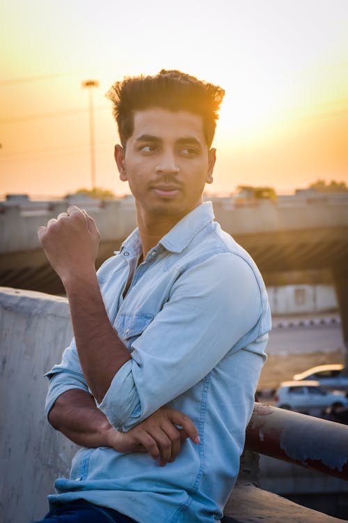 Homem Com Camisa Social Azul Chambray Inclinada Sobre Corrimão De Metal Cinza