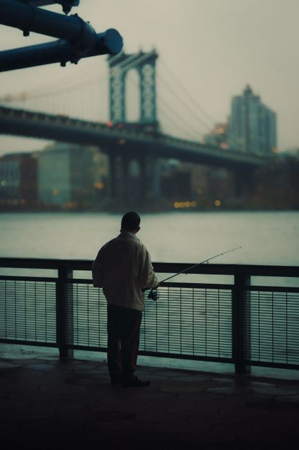 A man quietly fishes under the iconic Manhattan Bridge as evening descends.