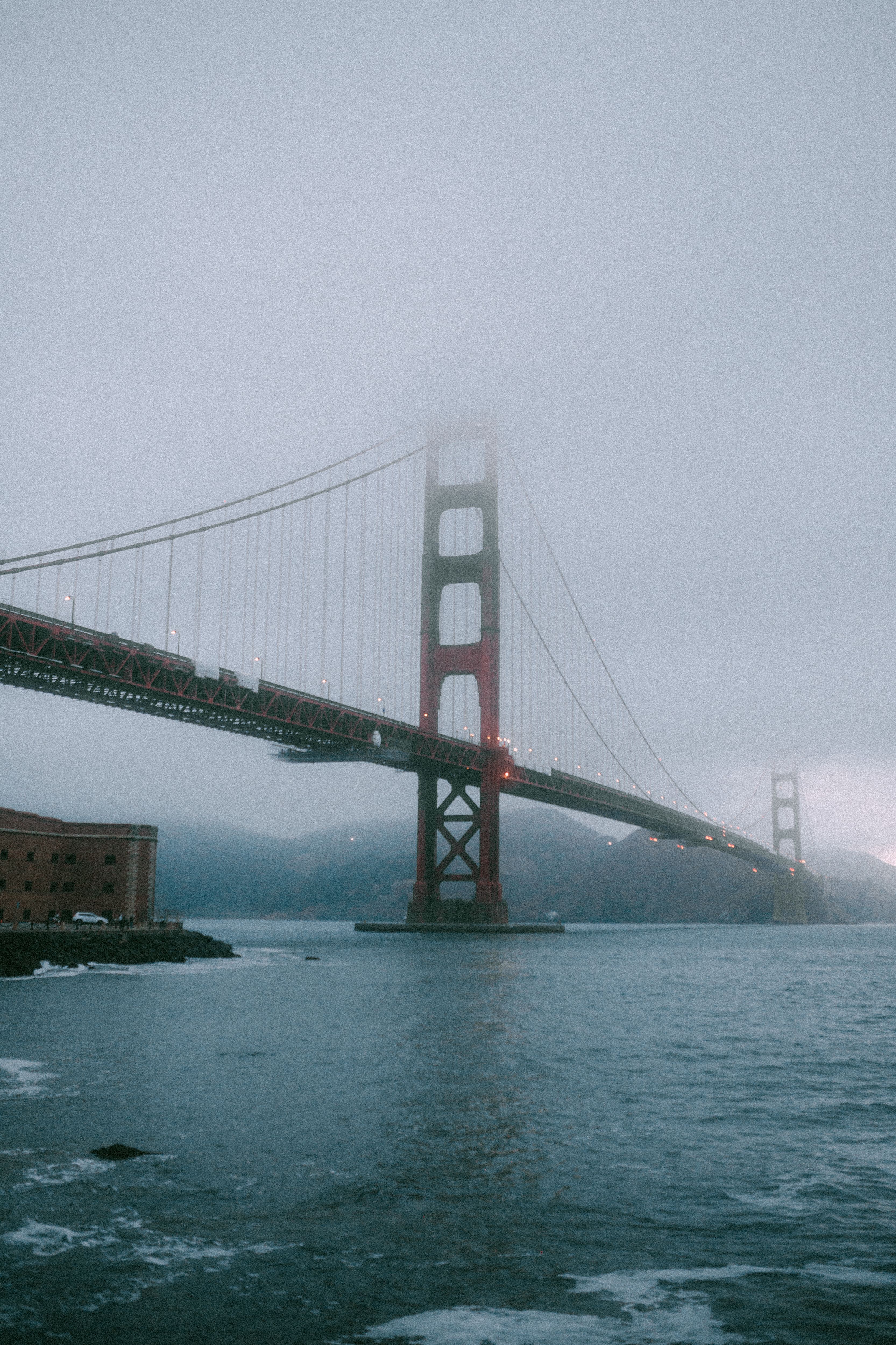 Mist shrouds the iconic Golden Gate Bridge in San Francisco, captured in a vertical composition.