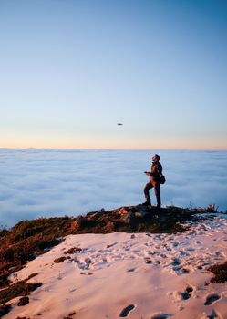 A person controls a drone on a snowy mountain, with a breathtaking sunset above the clouds.
