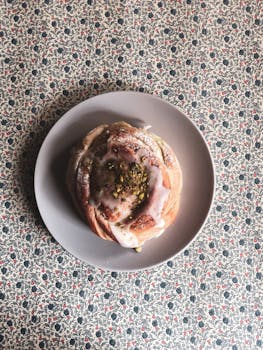 Delicious cinnamon roll topped with pistachios on a ceramic plate, perfect for food photography.