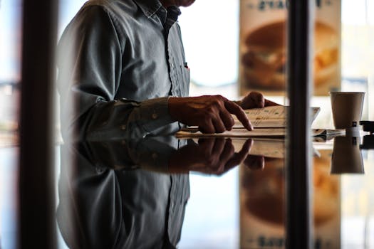 An adult man reads a newspaper indoors at a cafe, reflecting thoughtfully.