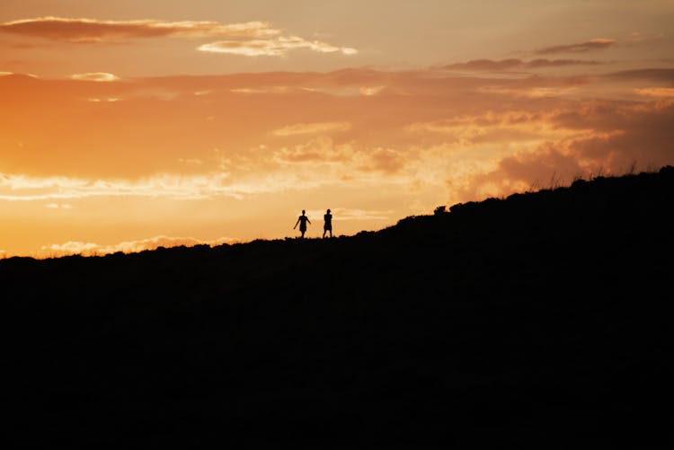 Silhouette Of Two People Walking On Hill During Sunset