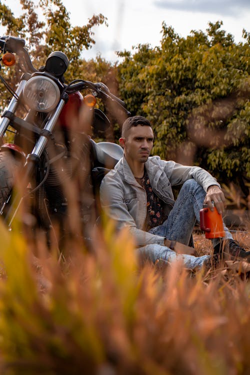 Man in Denim Jacket Sitting Beside the Black Motorcycle 