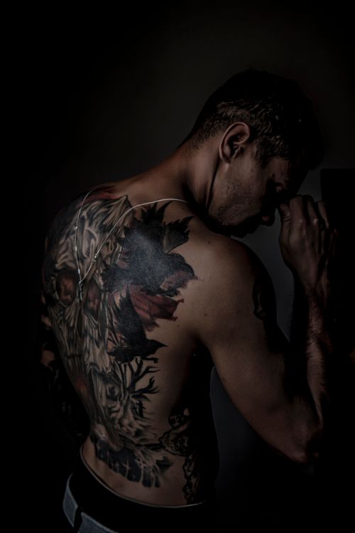 Free Moody studio shot of a shirtless man showcasing intricate back tattoos in low light. Stock Photo