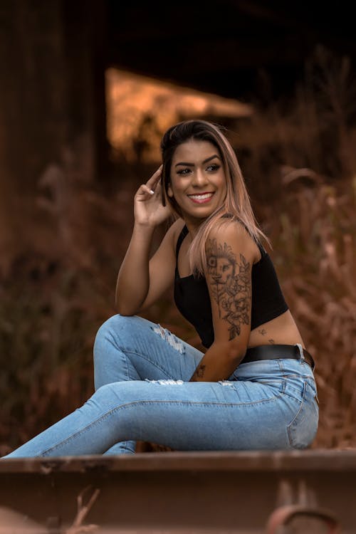 A Woman in Black Tank Top and Denim Jeans Sitting while Smiling