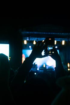 A crowd enjoys a live concert captured on a smartphone against a vibrant night backdrop.