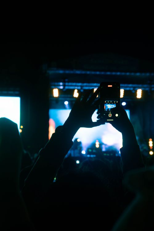 Free A crowd enjoys a live concert captured on a smartphone against a vibrant night backdrop. Stock Photo
