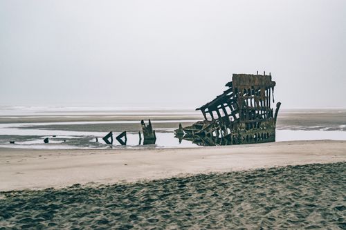 Free Rusted shipwreck on a sandy beach under an overcast sky, creating a moody, atmospheric scene. Stock Photo