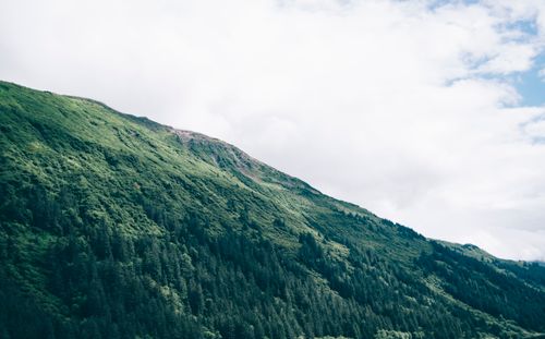 Free A stunning view of a lush green mountain side under a cloudy sky, showcasing the beauty of nature. Stock Photo