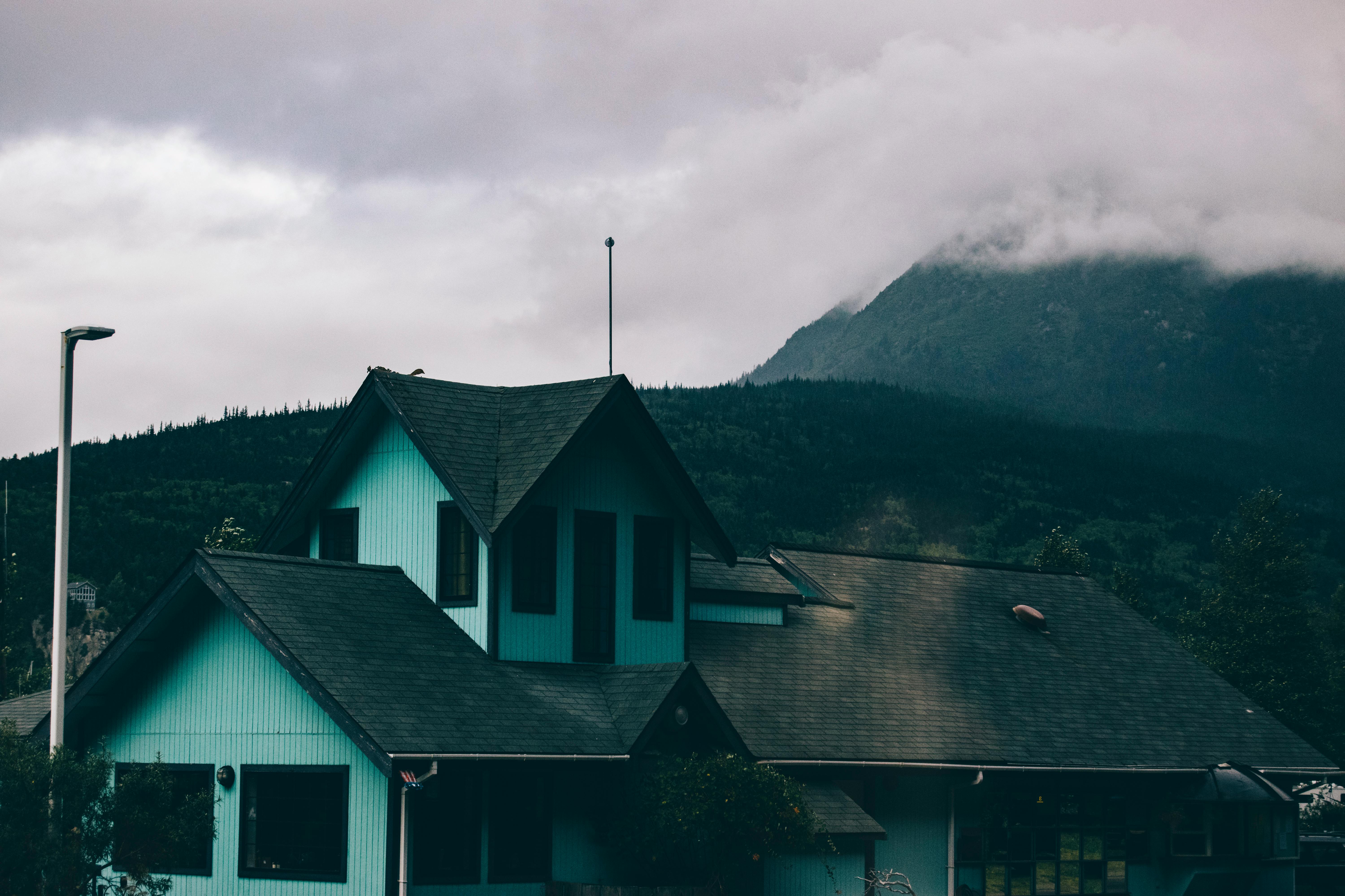 Blue and Black House Near Mountain Under Low Clouds · Free Stock Photo