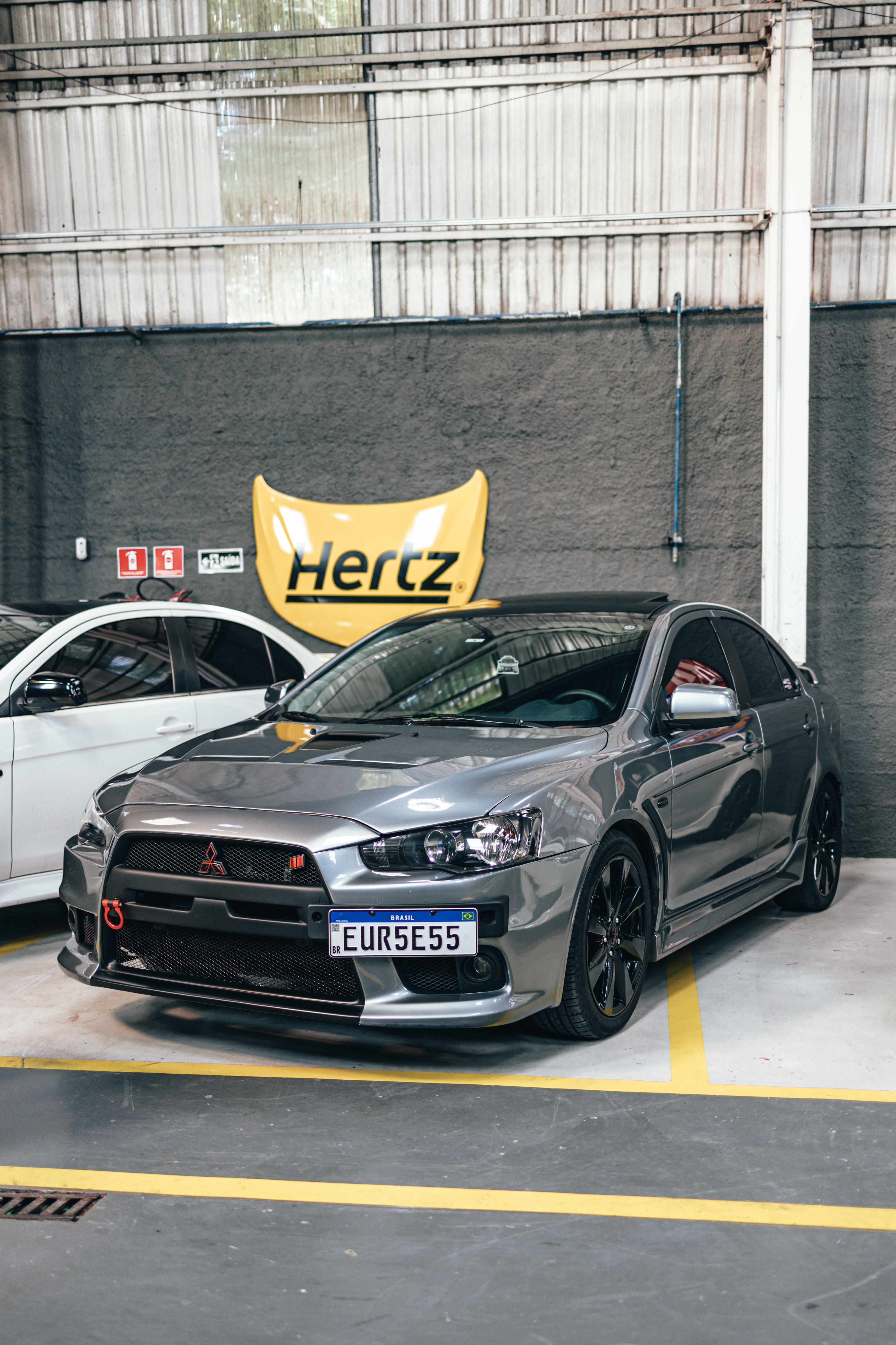 Gray Mitsubishi Evo parked in a well-lit indoor garage with Hertz signage in the background.
