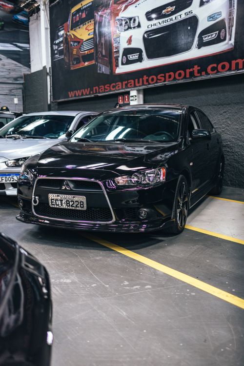 Free Sleek black sports car parked in an indoor garage next to other vehicles, under racing posters. Stock Photo