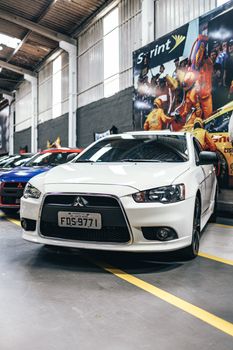 White sedan car parked in an indoor garage with a racing-themed mural behind.