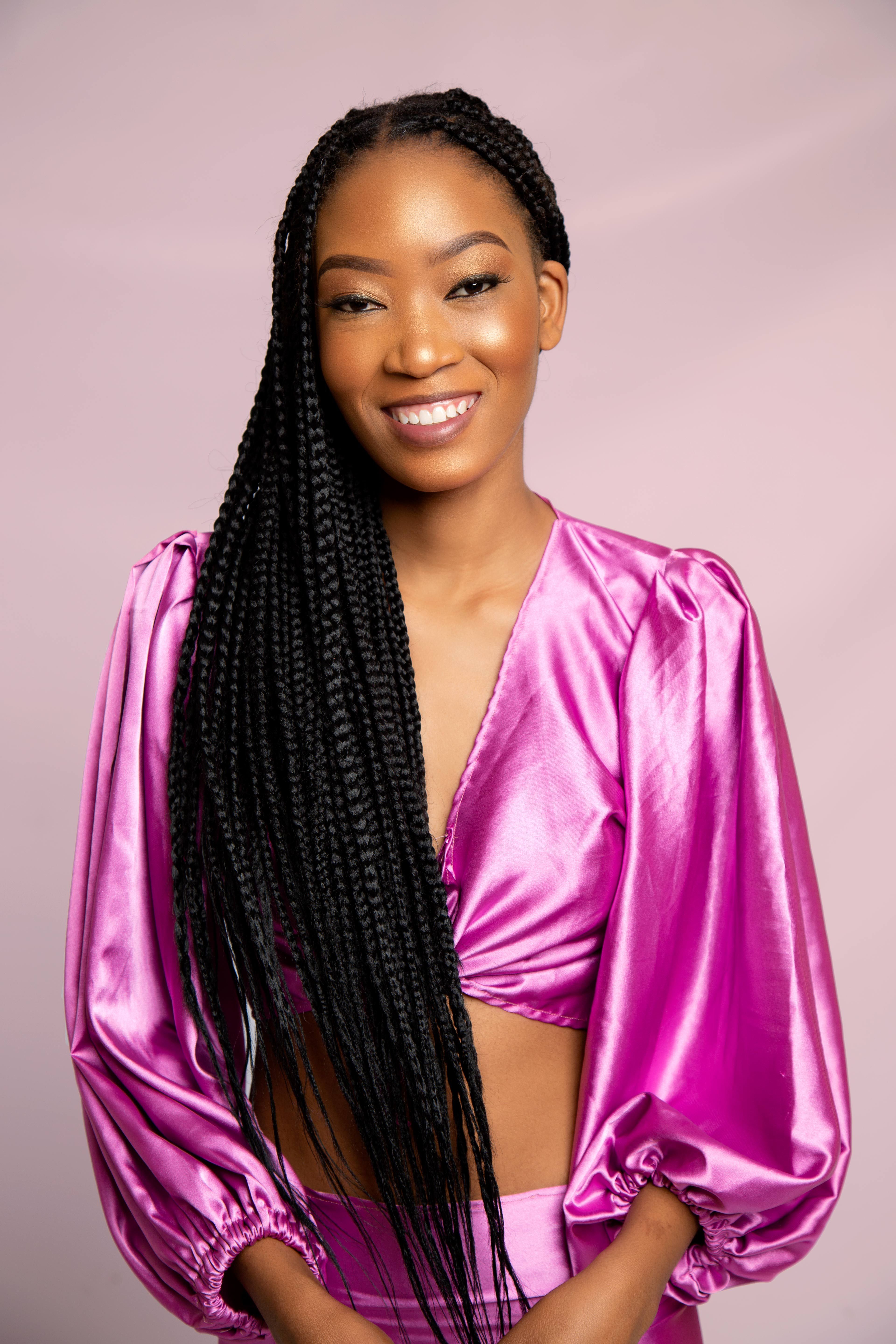 Beautiful woman with long braided hair in vibrant pink top, smiling confidently.