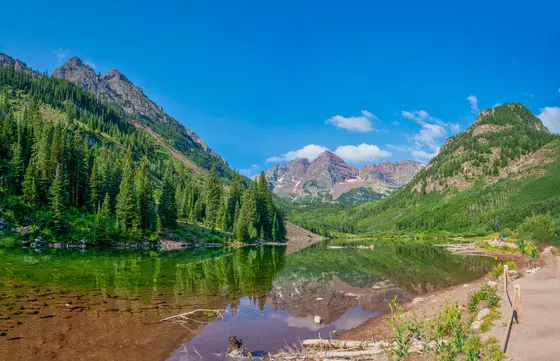 Stunning reflection of Maroon Bells in the tranquil lake under a vibrant blue sky in Colorado.