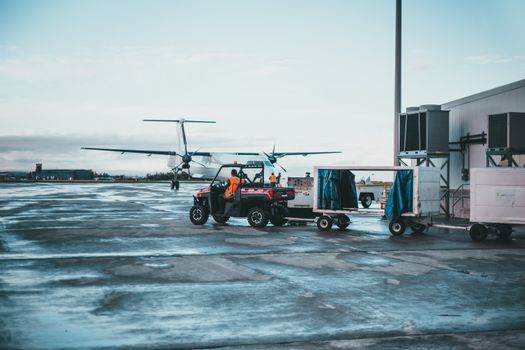 View of airport crew managing luggage near airplane at dawn.