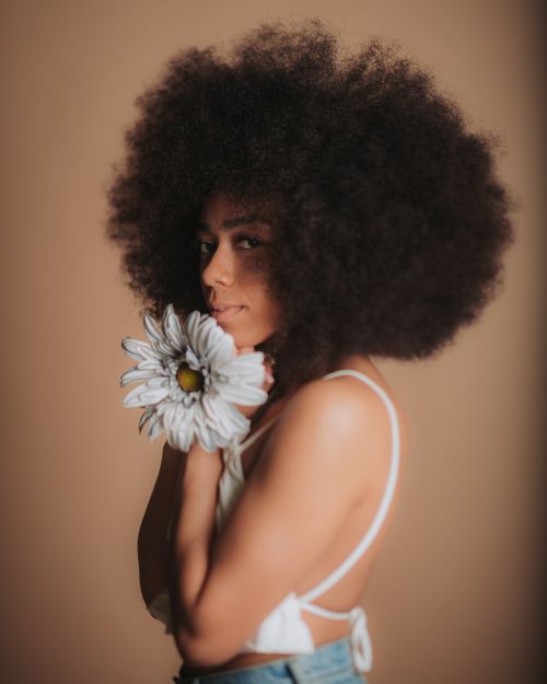 Free A beautiful portrait of a woman with afro hair holding a white flower against a neutral background. Stock Photo