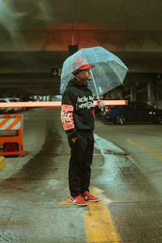 Man in hoodie holding transparent umbrella in a parking garage on a rainy day.