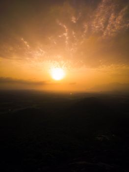 A breathtaking golden sunset illuminates the sky with scattered clouds over a serene hilly landscape.