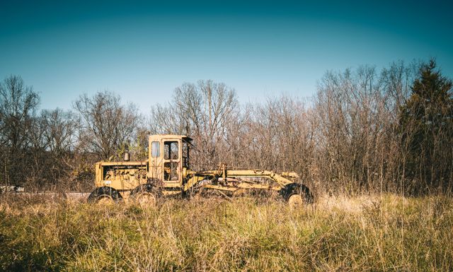 Engin de chantier abandonné au milieu d'un terrain envahi par de hautes herbes