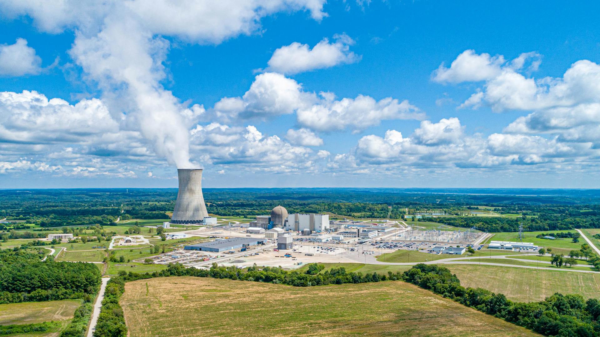 Aerial view of Callaway Nuclear Plant with cooling tower amidst lush landscape under a blue sky.