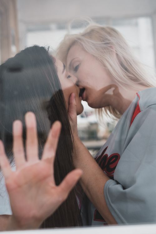 Free Two women sharing an intimate kiss through a glass window, showcasing love and tenderness. Stock Photo