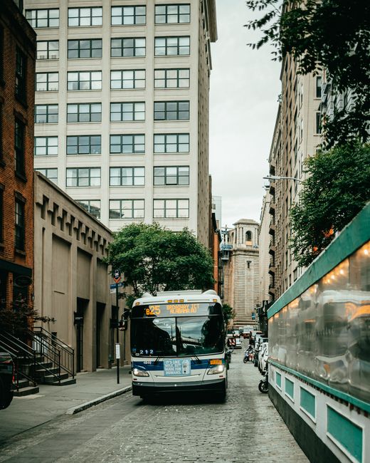 Public bus driving through a street in New York City's urban landscape with high-rise buildings.