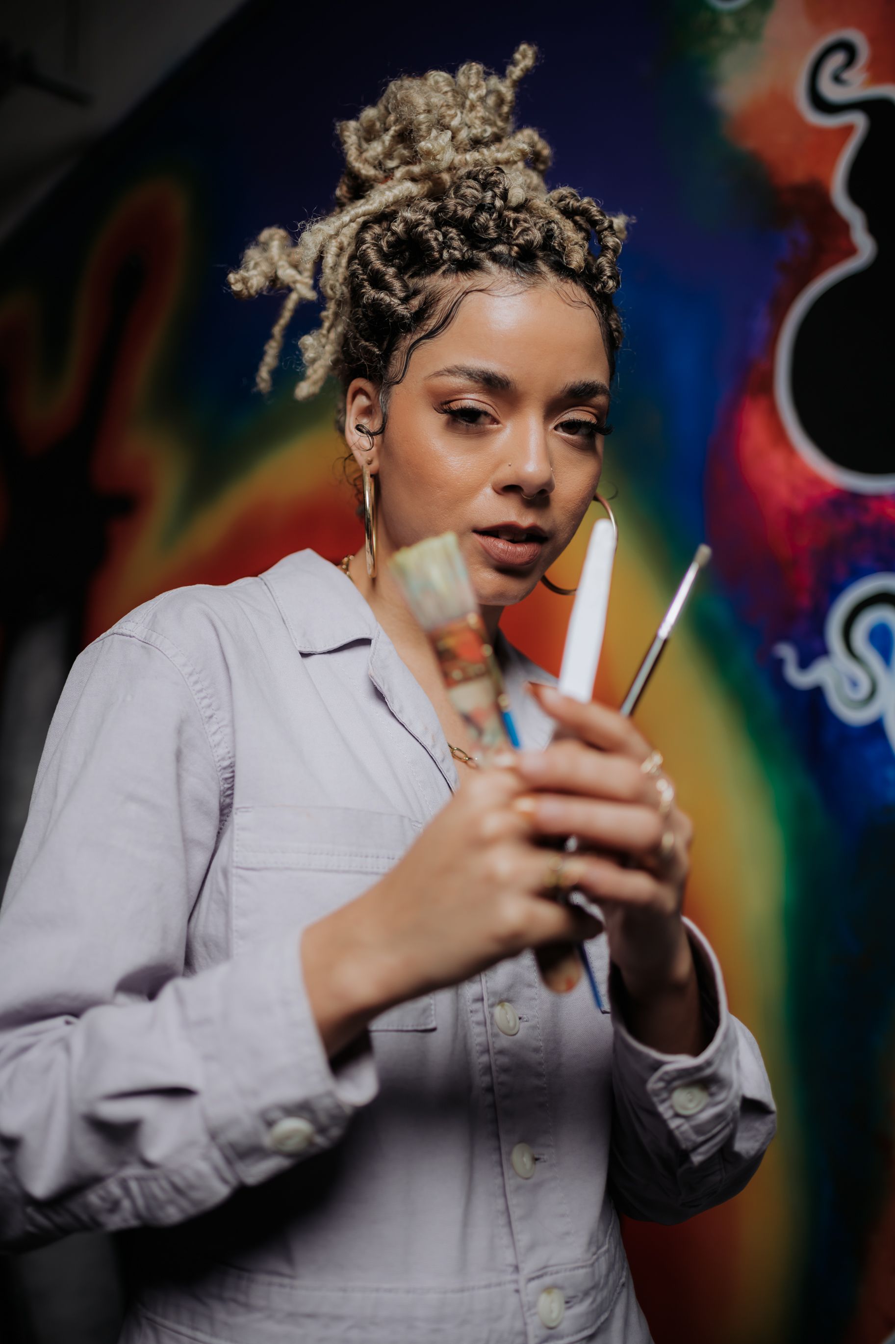 African American artist holding paintbrushes in a vibrant studio setting.