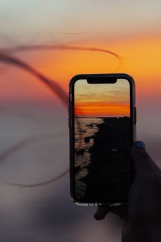 A smartphone with sunset reflection on a beach, showcasing vibrant colors.