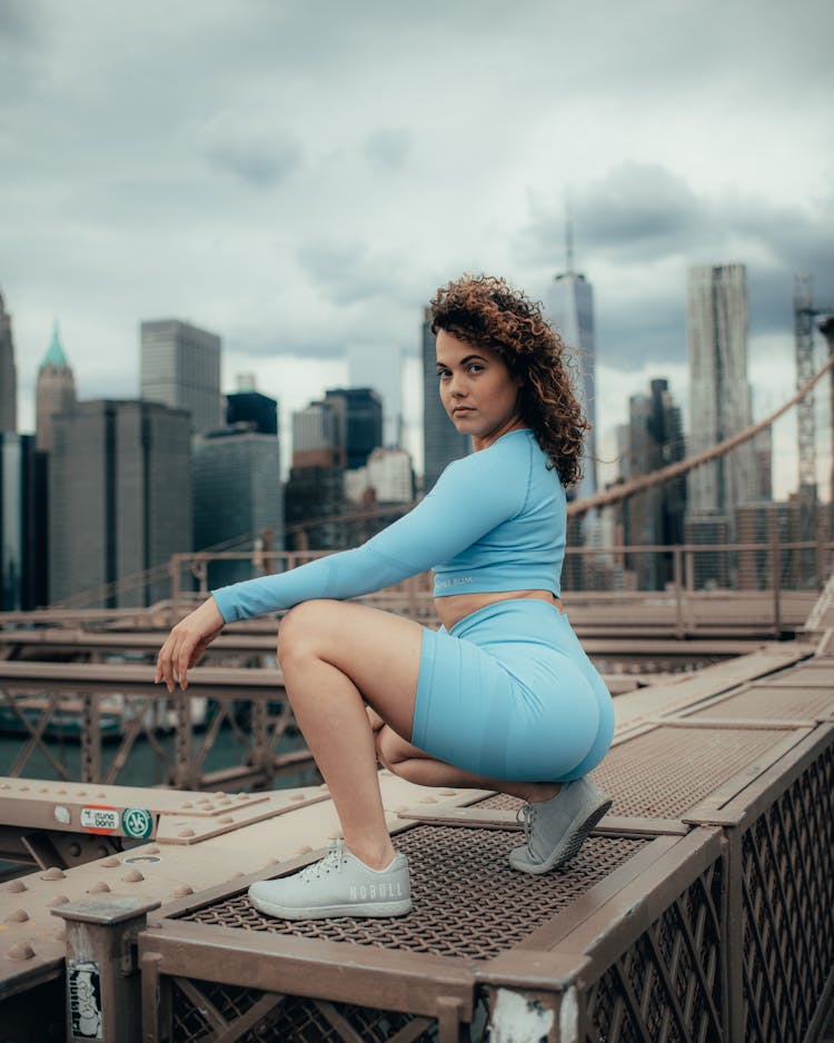 Woman In Sport Clothes Sitting And Posing On Bridge