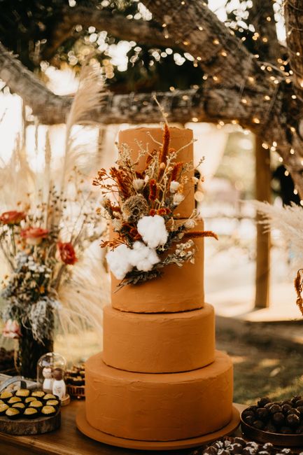 Rustic themed wedding cake adorned with floral arrangements at an outdoor reception.