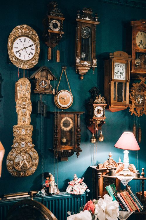 Free A charming collection of vintage wall clocks on a teal wall in a cozy, warmly lit room. Stock Photo