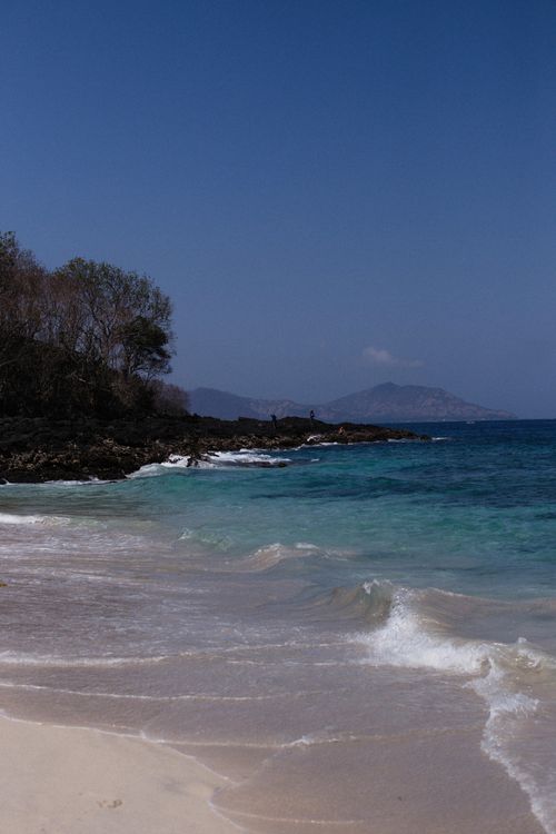 Free A tranquil beach with rocky shoreline, waves gently reaching the sandy coast under a clear blue sky. Stock Photo