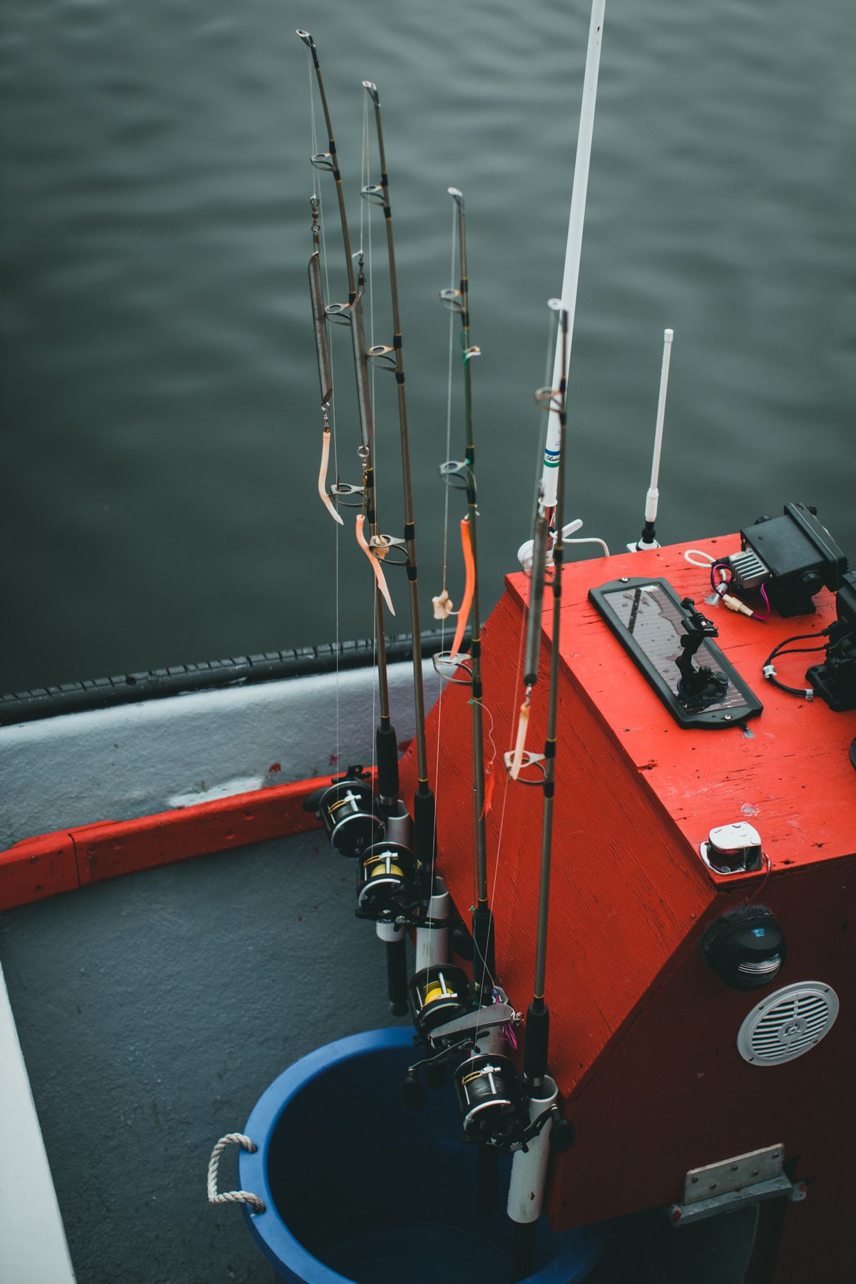 Fishing rods secured in holders on a red boat over calm water