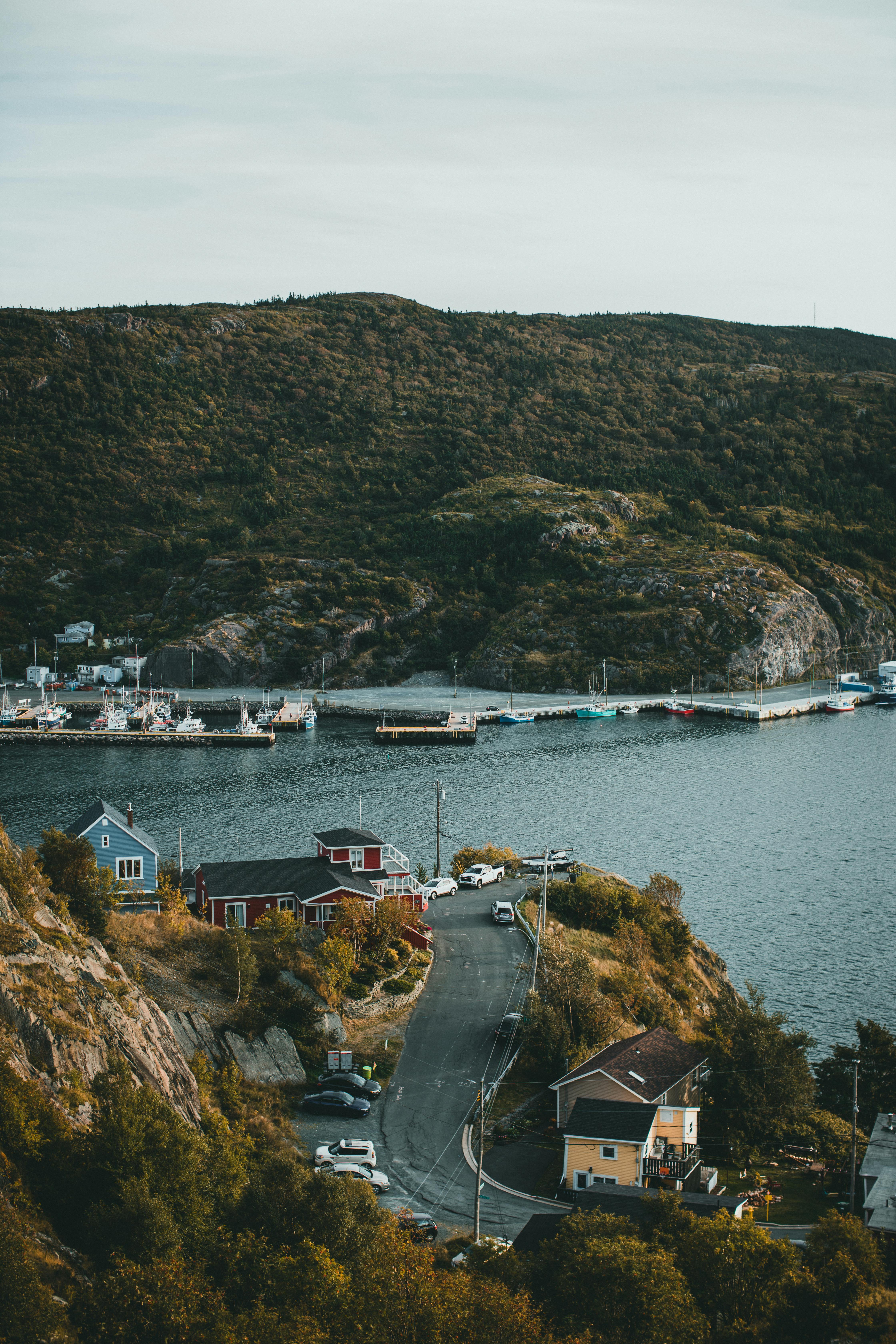 A serene coastal village with boats docked by the bay and lush green hillside backdrop.