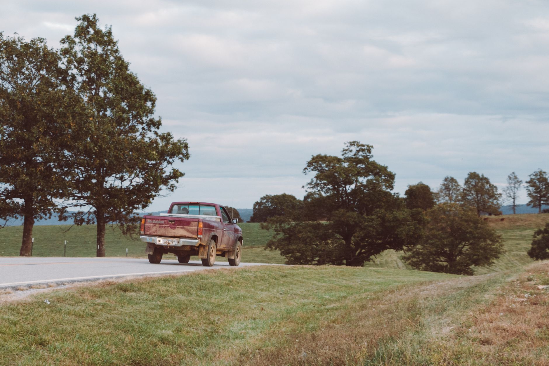 A pickup truck drives on a scenic road in Arkansas, surrounded by vibrant green grass fields and trees.