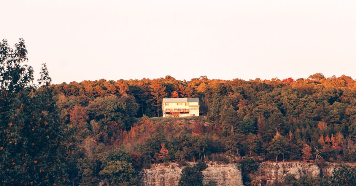 A secluded house sits atop a cliff surrounded by vibrant autumn foliage in Arkansas.