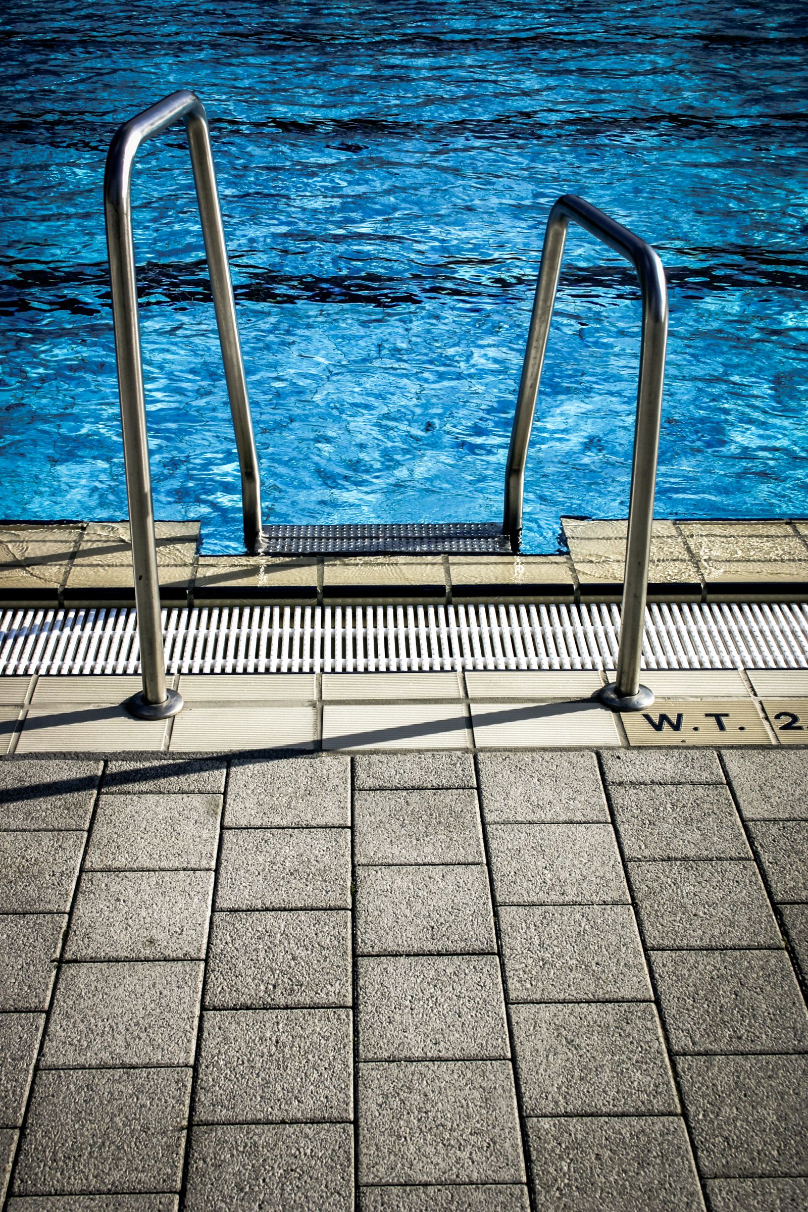 A steel pool ladder above deep blue water and a tiled pool edge