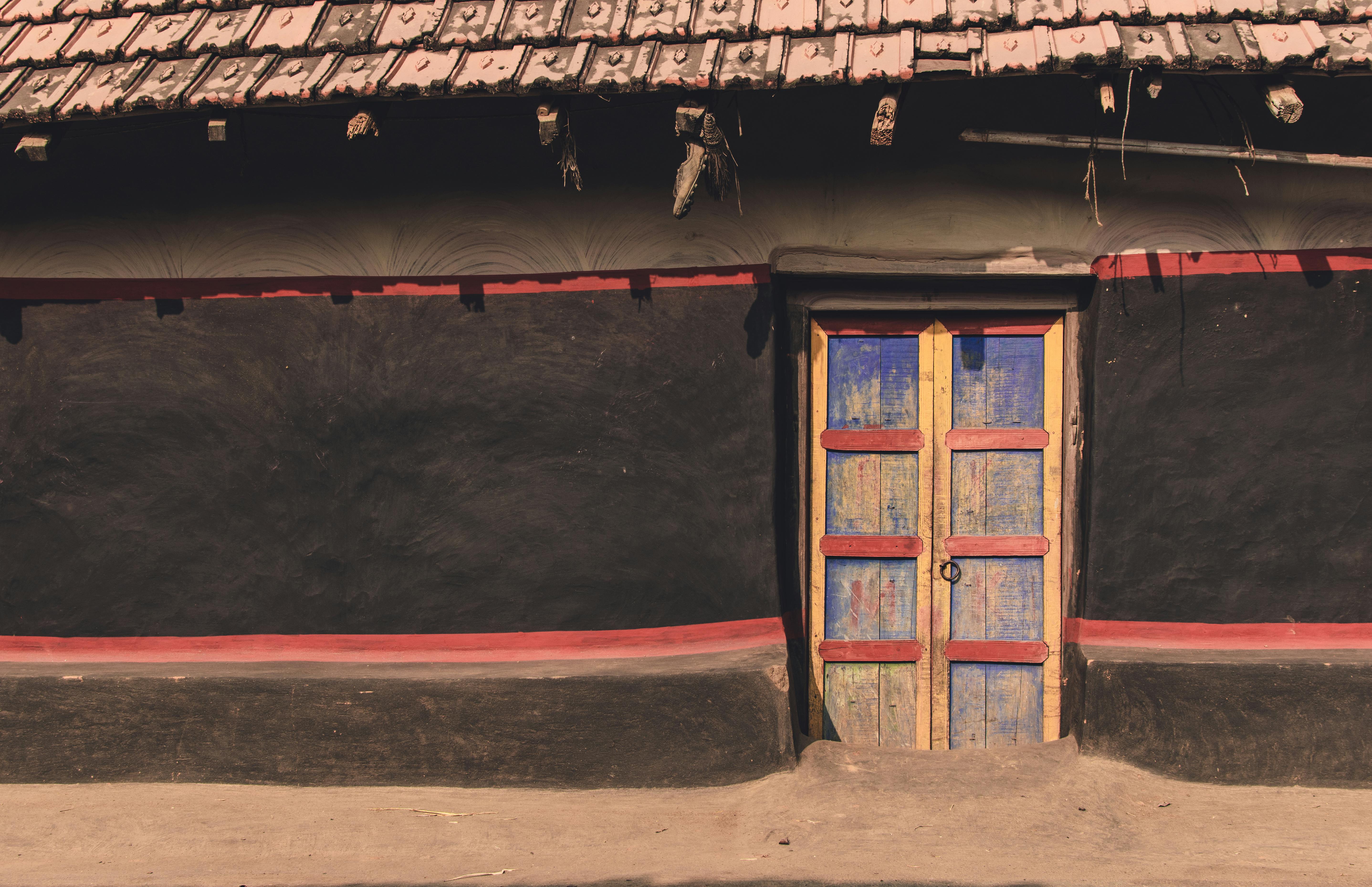 Rustic village house in India with a vibrant blue-painted wooden door and red accents.