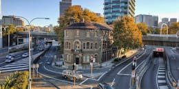 悉尼一座历史建筑矗立在繁忙的十字路口，背景中是川流不息的交通与摩天大楼