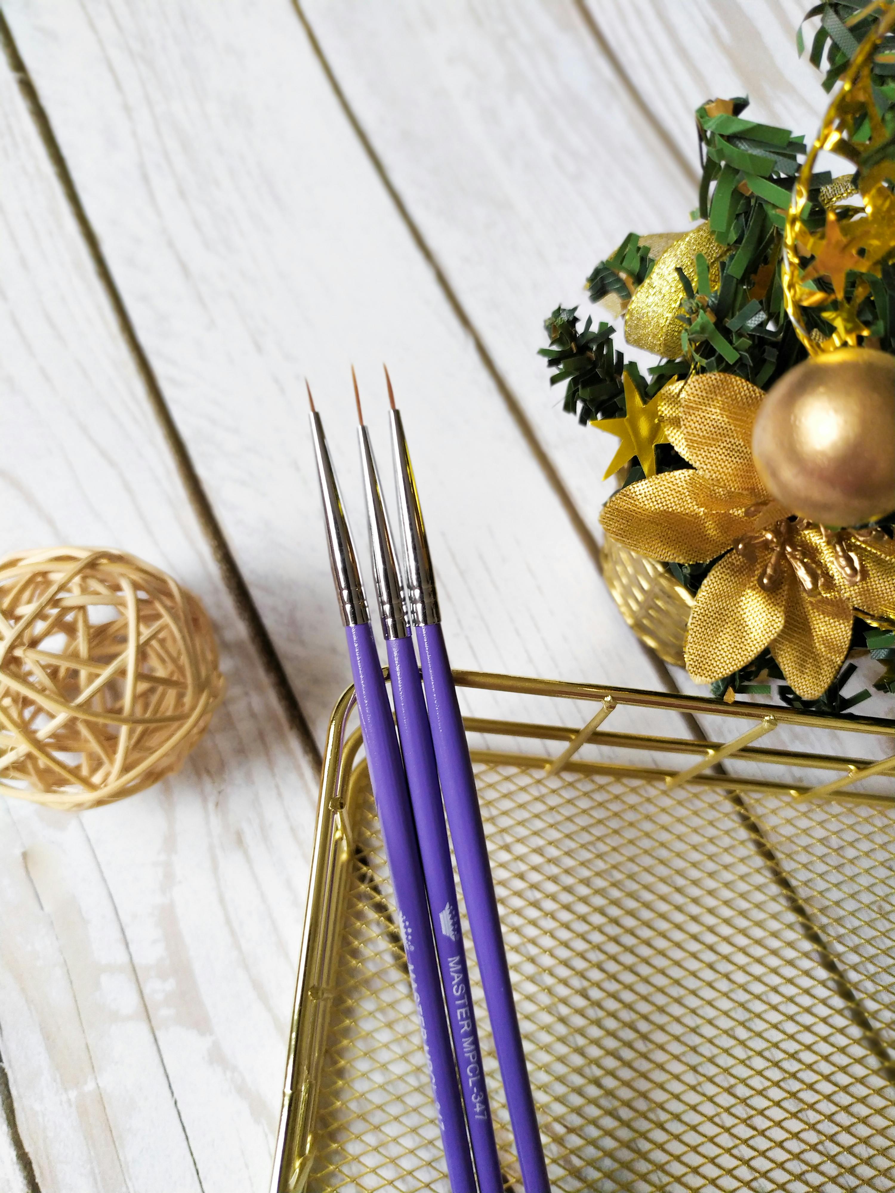 Colorful paintbrushes and Christmas decorations on a wooden surface, perfect for holiday craft ideas.