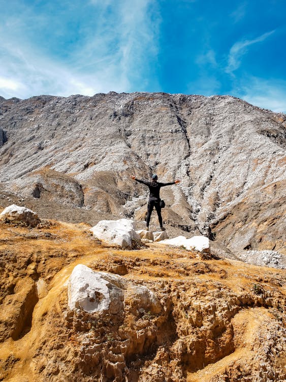 Person with Arms Wide Open Standing Near the Rock Mountains 