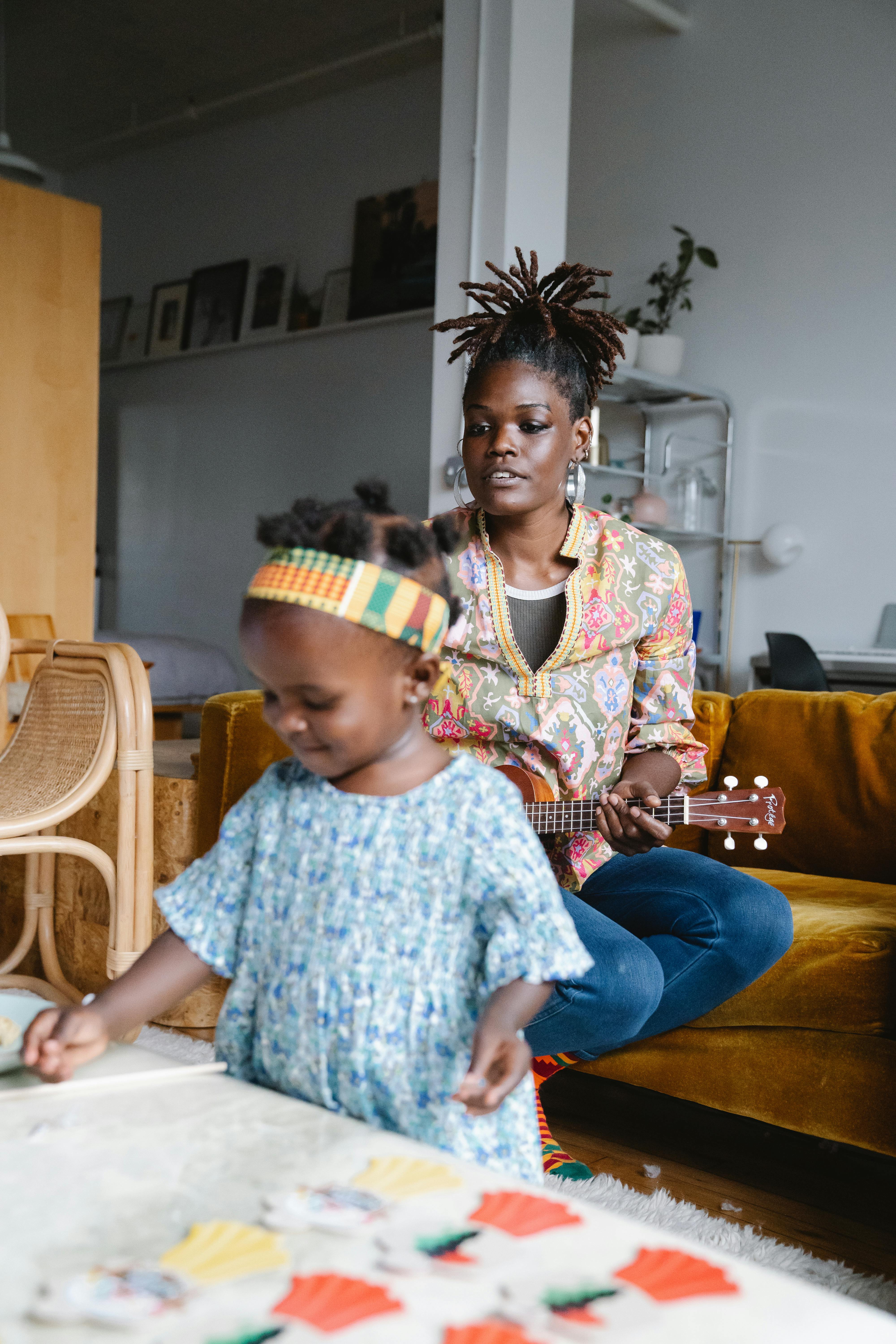 Mother playing ukulele while her daughter engages in creative play, capturing a warm family moment indoors.