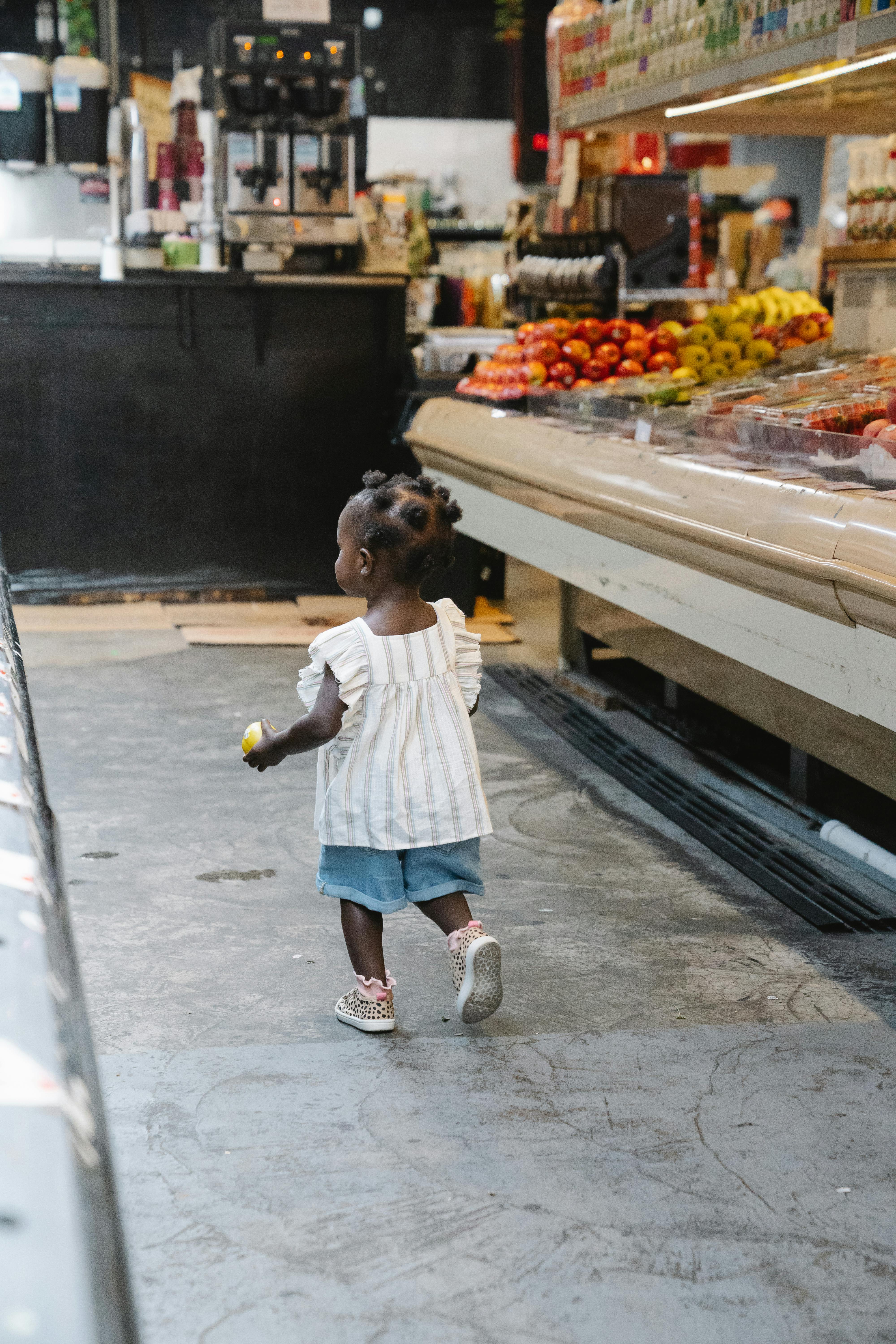 A young girl exploring a grocery store aisle with colorful produce displayed.